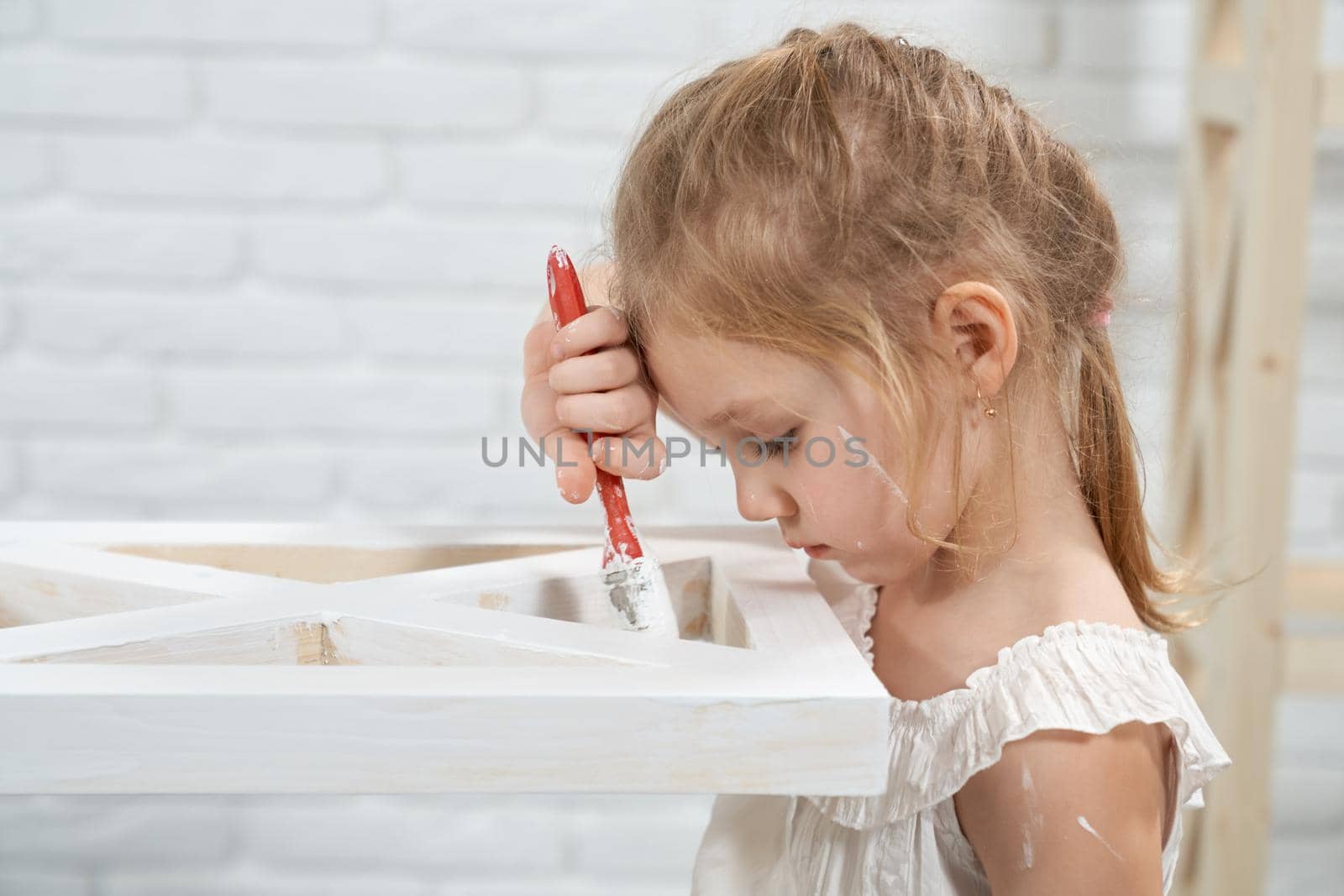 Cute little girl painting wooden rack at home. by SerhiiBobyk