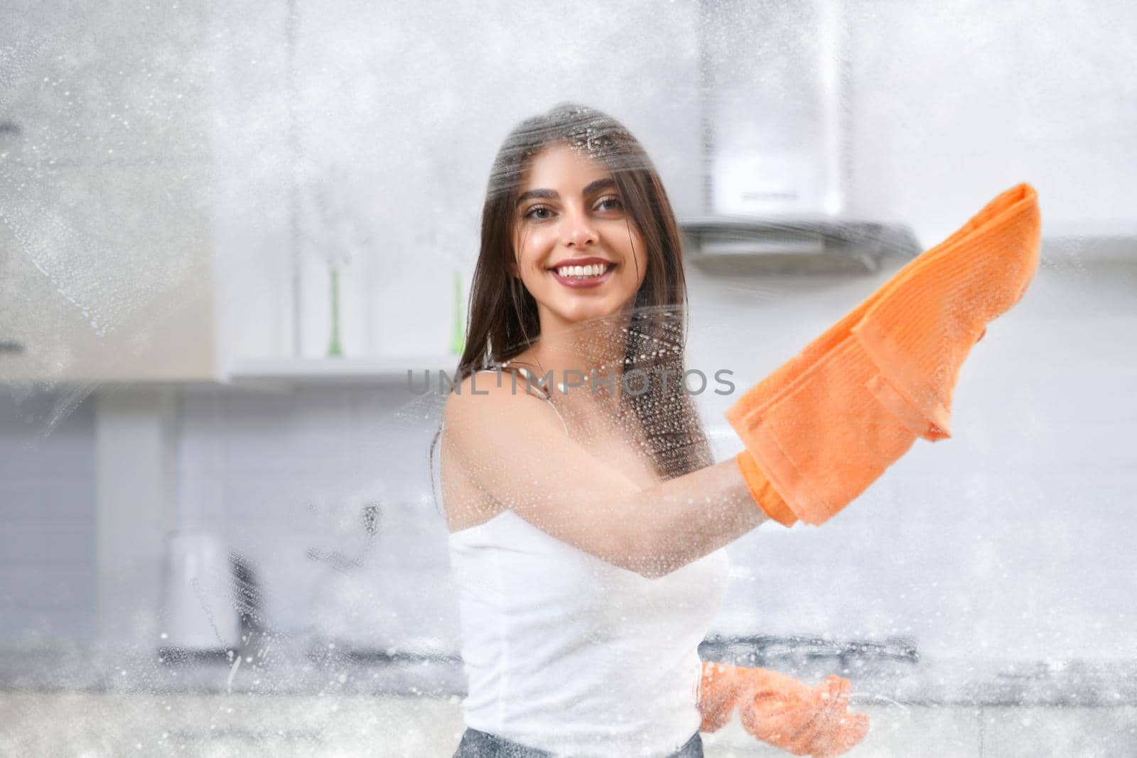 Close up of beautiful woman smiling and washing window with rag. Concept of house cleaning.