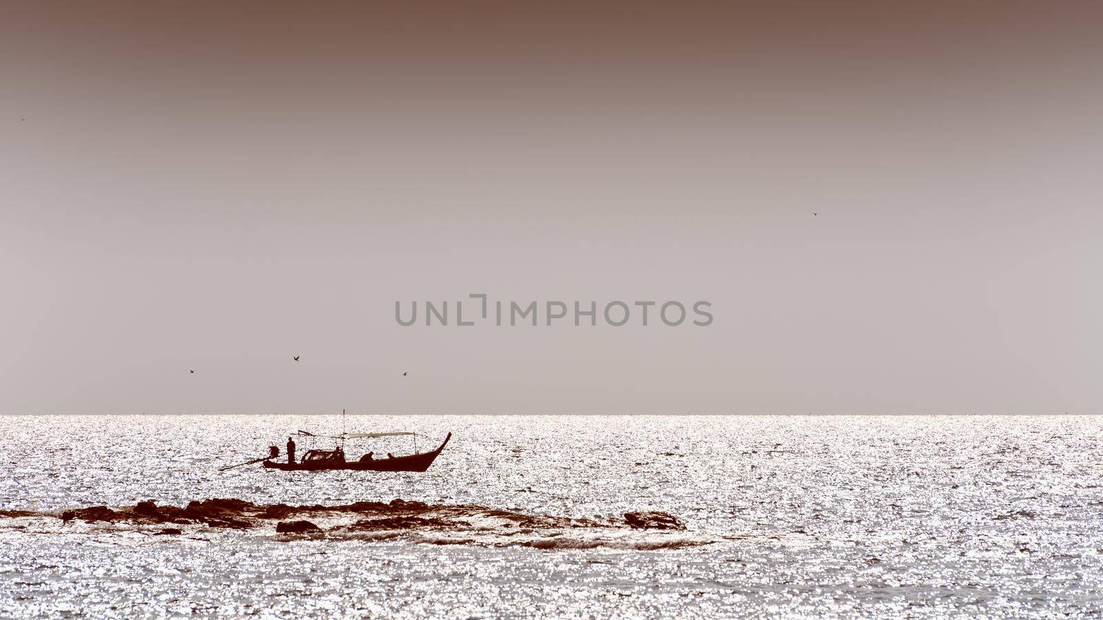 Silhouette small fishing boat and native fisherman on the sea, beautiful landscape of the coastal at Koh Tarutao, Satun, Thailand in sepia two tone colors, 16:9 wide screen