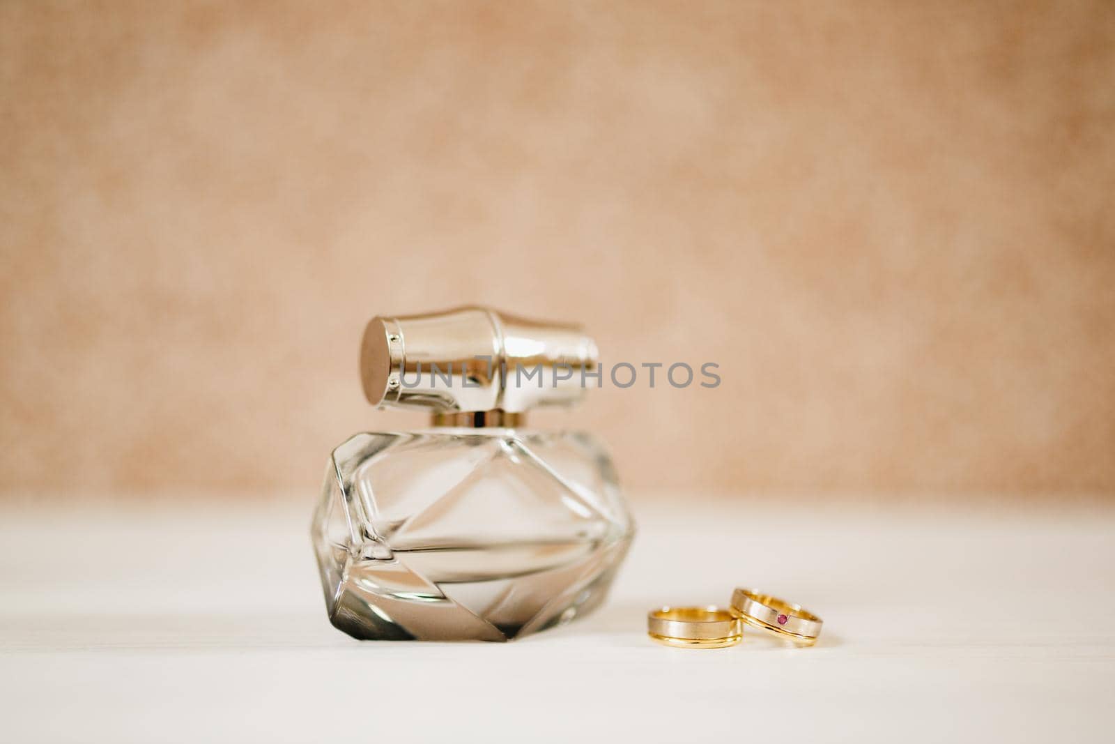 Perfume bottle and gold wedding rings of the bride and groom on a light background. High quality photo