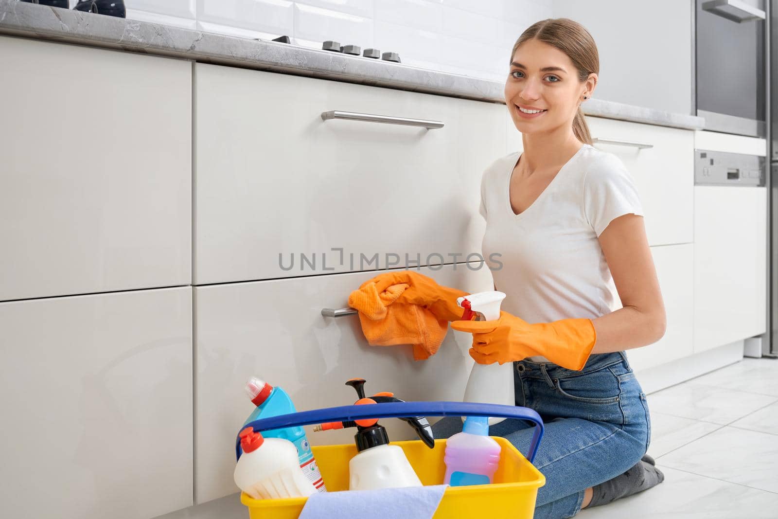 Smiling young woman holding rag and detergent in kitchen. by SerhiiBobyk