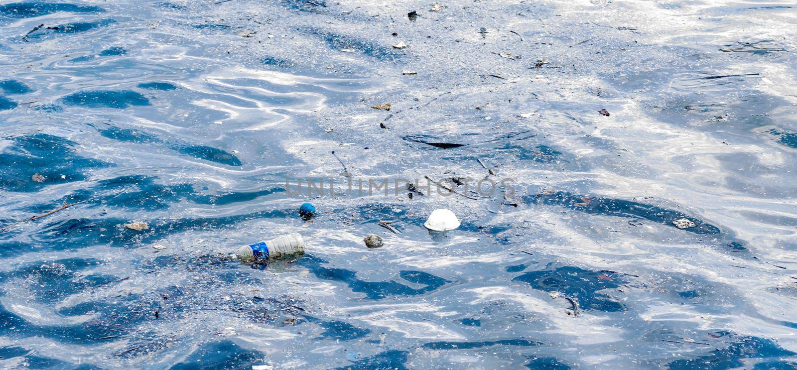 plastic bottled water floating on a beach side and other flowing plastic garbage by billroque
