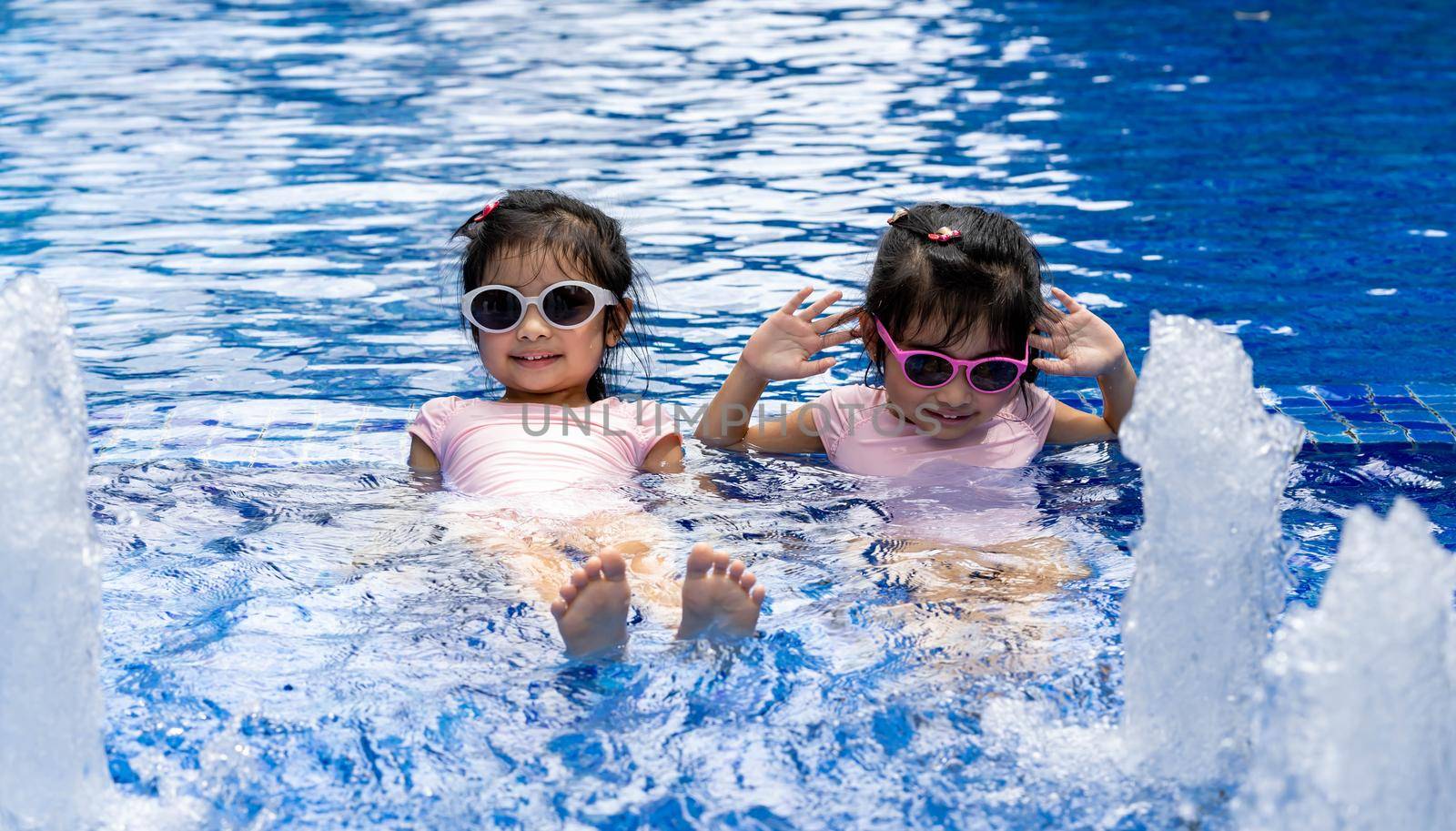 Portrait of pretty asian twins smilling and posing on swimming pool background wearing pink swim suit and sun glasses by billroque