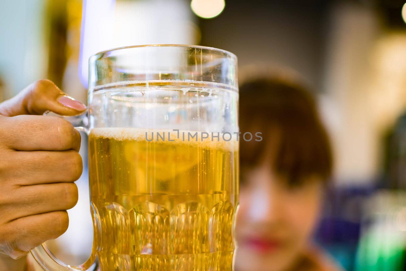 Beer in a glass and a girl holding it and saying cheers.