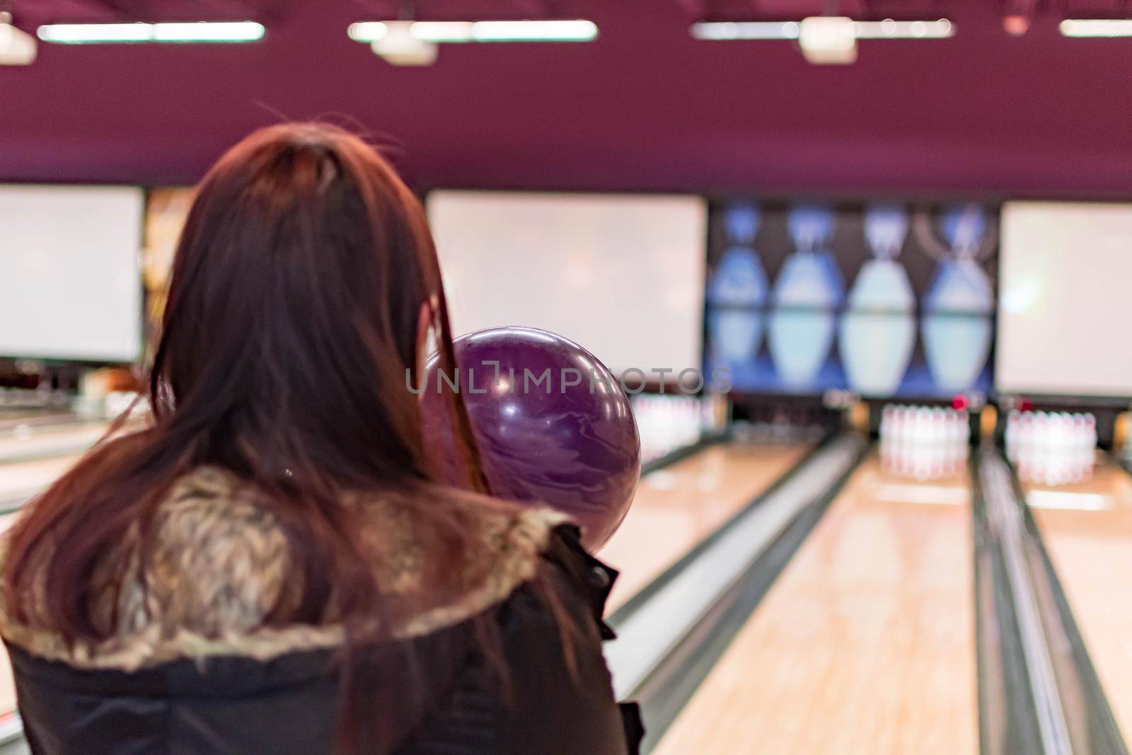 A bowling ball while being aimed to the target by a female adult in a bowling tournament. Purple  bowling ball and blurry bowling alley background by billroque