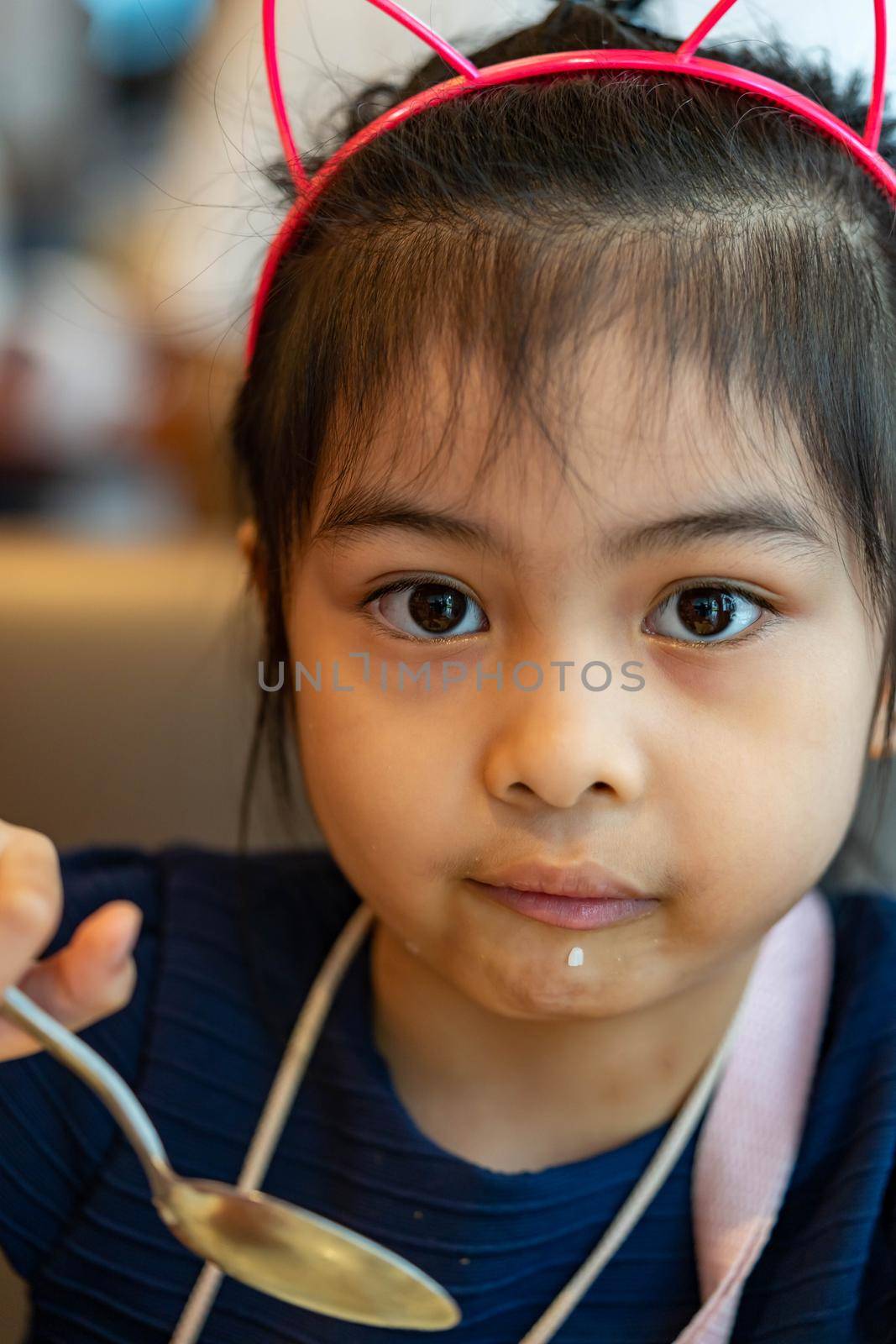 Female asian child while eating rice using spoon. Child enjoys eating rice by her own. Child learning to use spoon and eat by her own