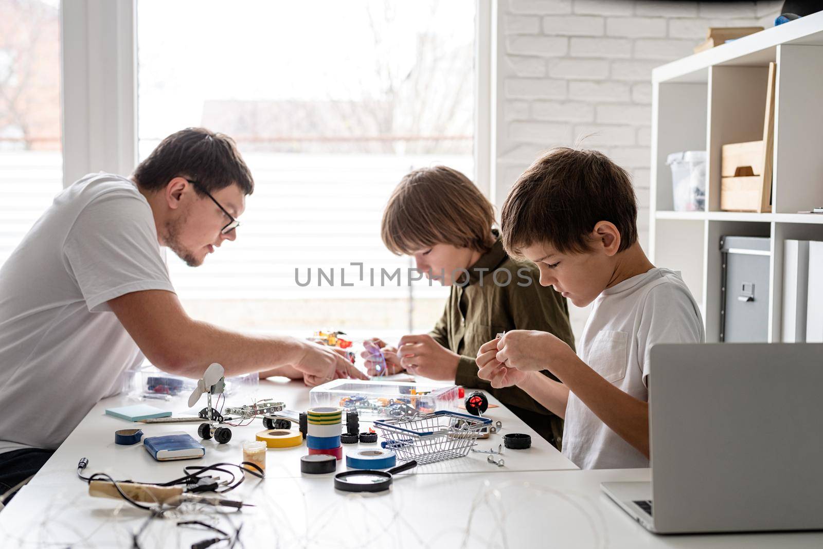 Young boys and teacher having fun constructing robot cars at the workshop by Desperada