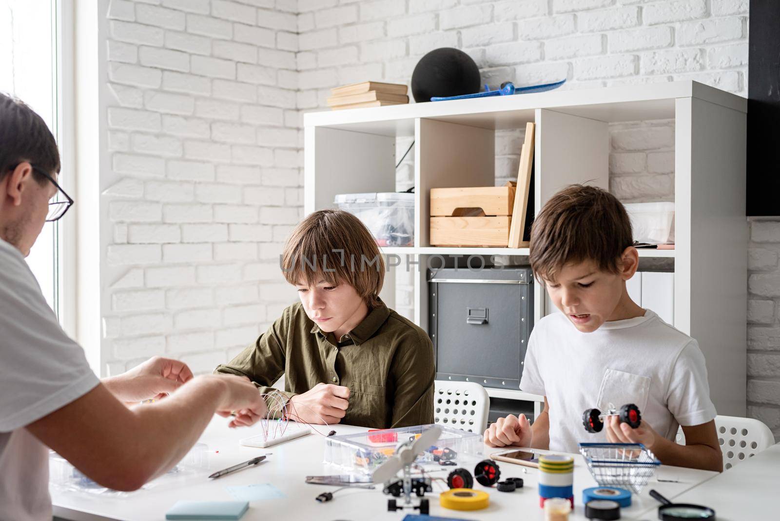 Young boys and teacher having fun constructing robot cars at the workshop by Desperada