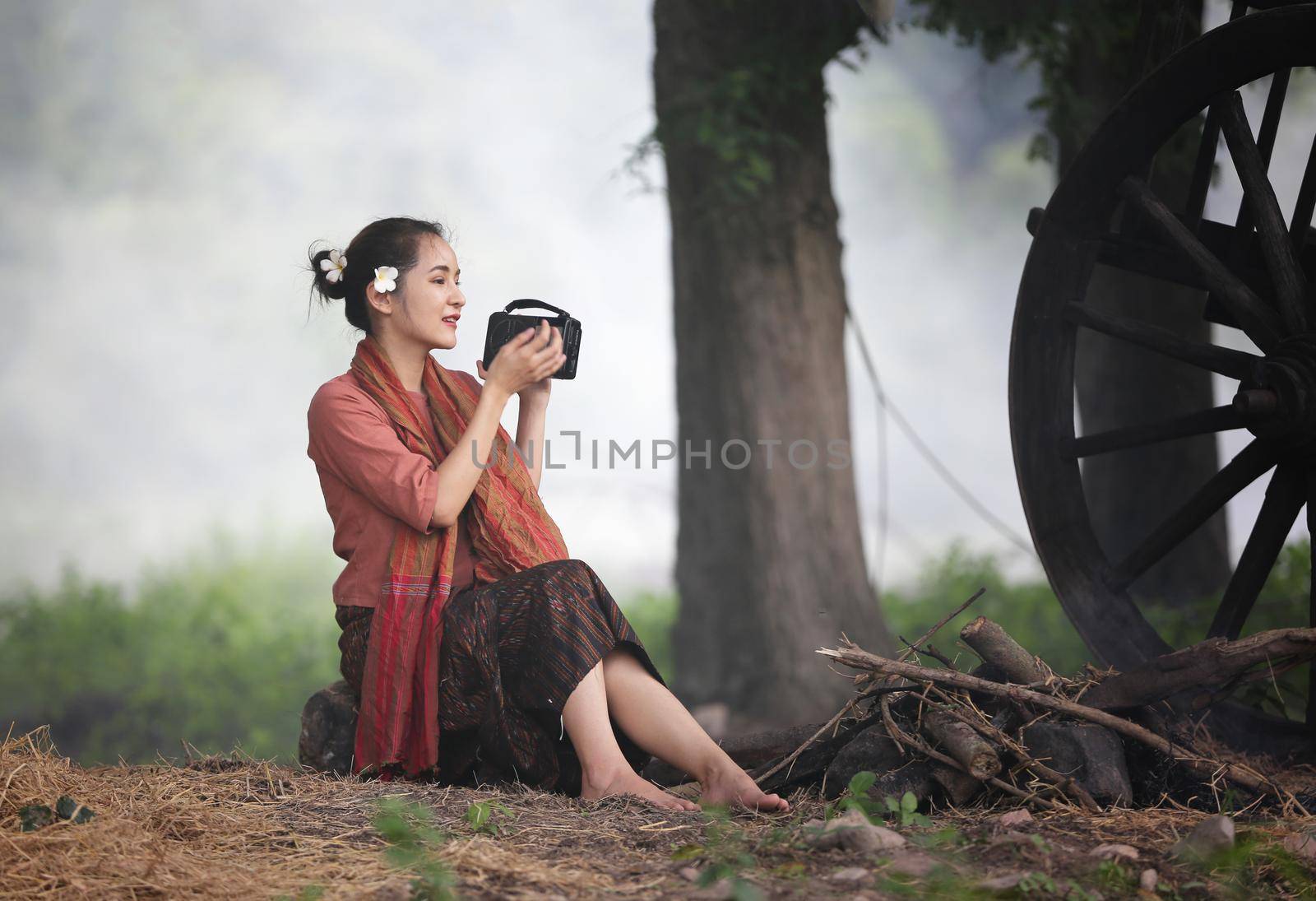 Asian woman wearing traditional thai culture, in field, vintage style listening radio on buffalo and farm background