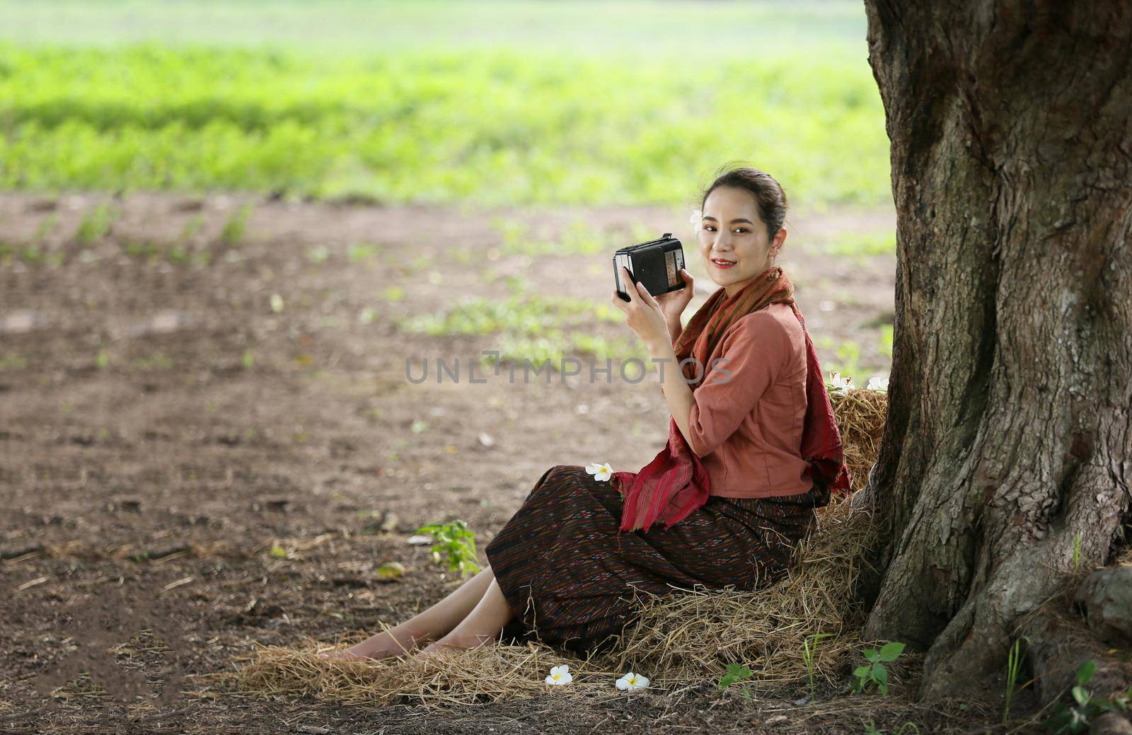 Asian woman wearing traditional thai culture, in field, vintage style listening radio on buffalo and farm background
 by chuanchai