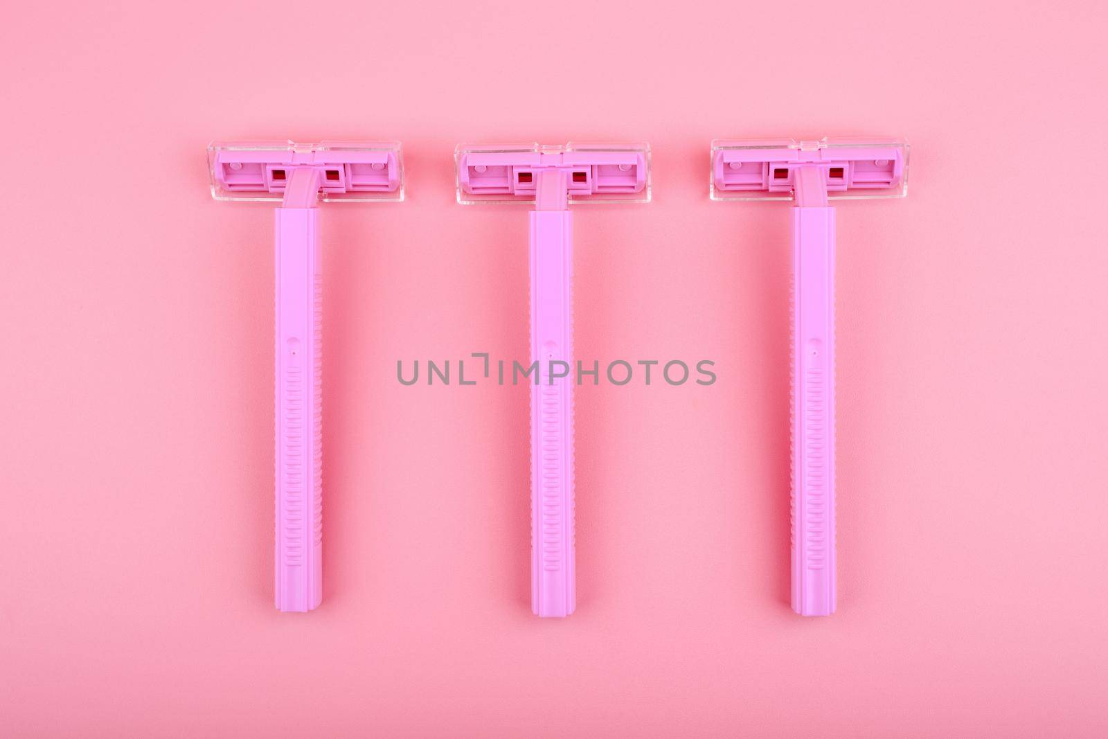 Top view of three pink razors in a row against pink background. Concept of smooth skin, shaving and epilation