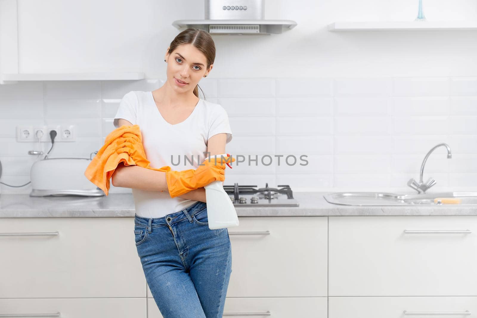 Young woman standing in modern kitchen with rag and detergent. Concept of preparing for cleaning kitchen.