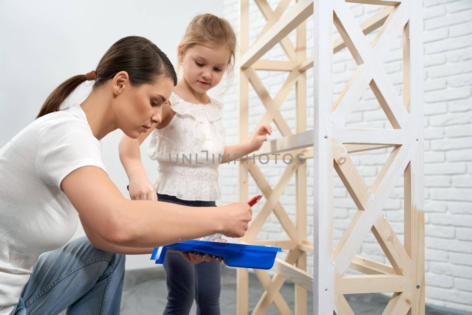 Close up young mother showing daughter how painting wooden rack at home. Concept of family time and repair at home.