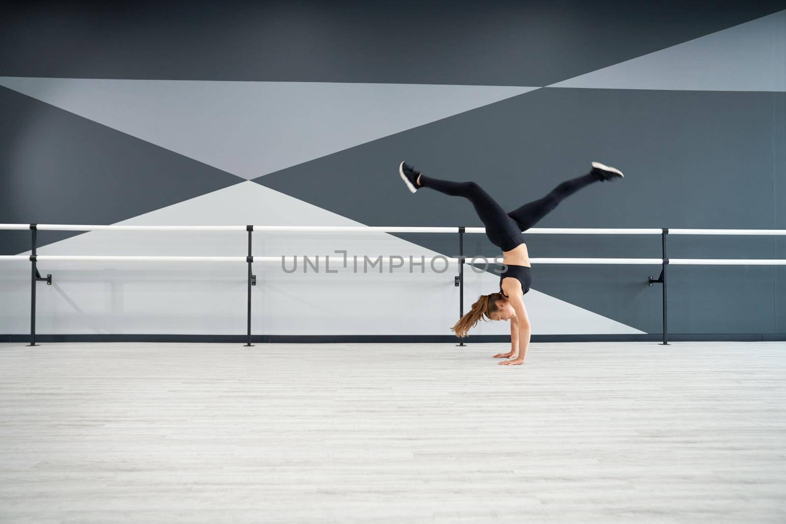 Female dancer practicing wheel jump in dance hall. by SerhiiBobyk