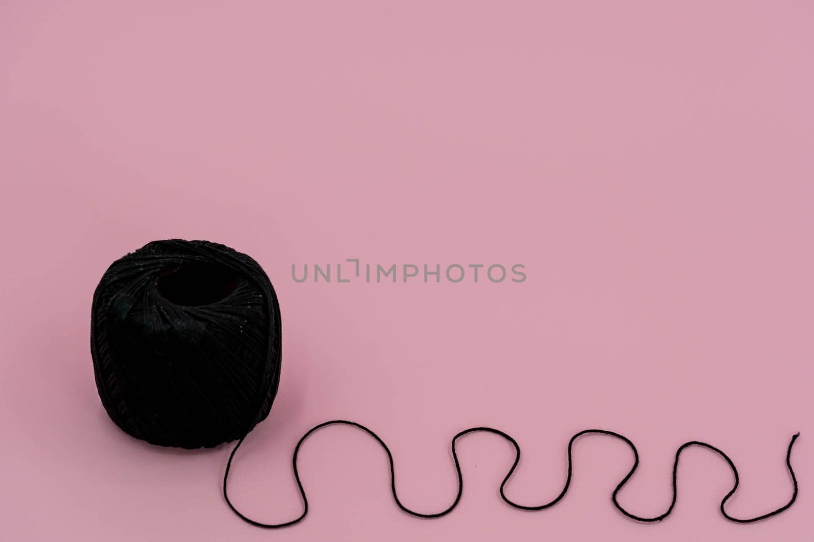 A ball of black braided small robe, made from synthetic yarn, for tying up something, for pink background.