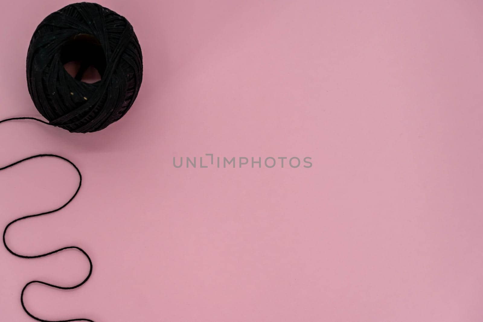 Black ball thread. A ball of black braided small robe, made from synthetic yarn, for tying up something, for pink background.