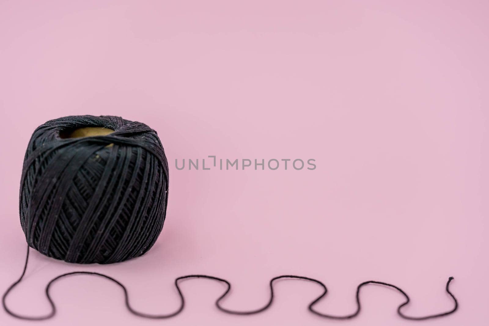 Black ball thread. A ball of black braided small robe, made from synthetic yarn, for tying up something, for pink background.