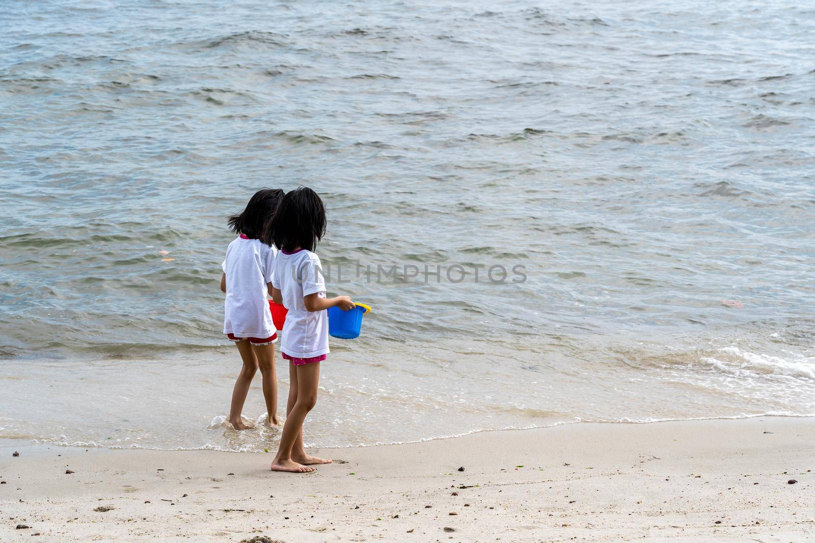 two little girls sitting by the edge of ocean on a sandy beach