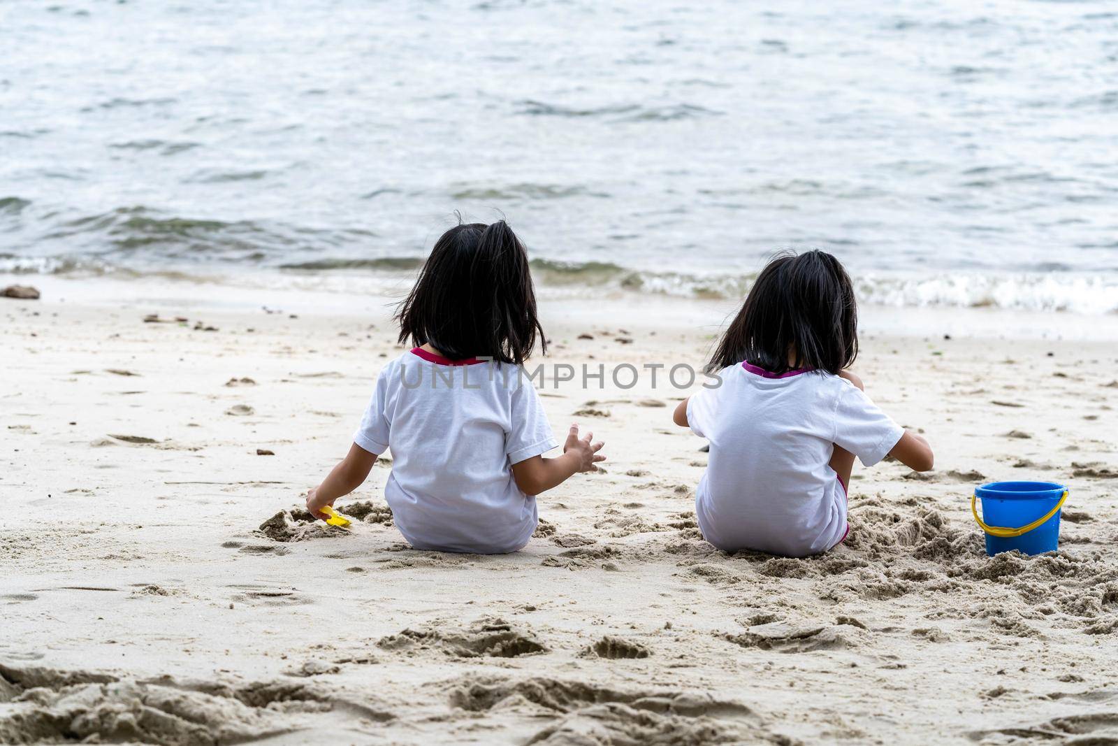 Sisters while sitting on the sand and playing with sand and beach toys by billroque