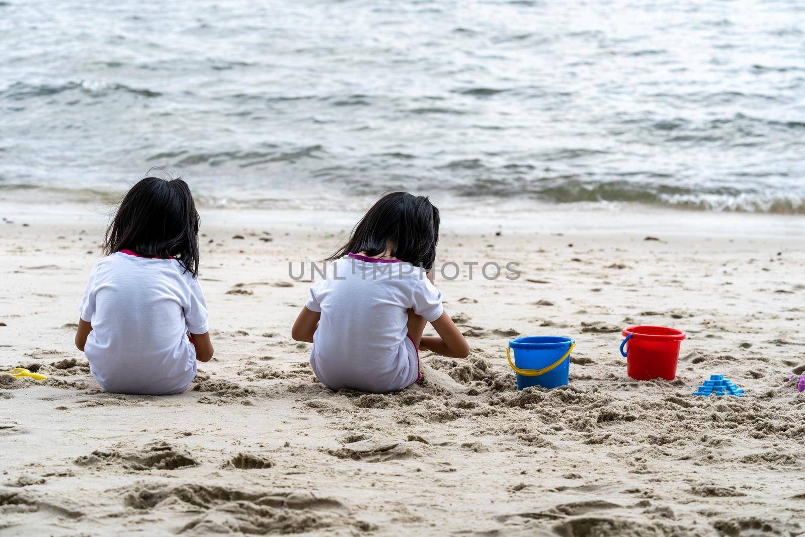 Sisters while sitting on the sand and playing with sand and beach toys