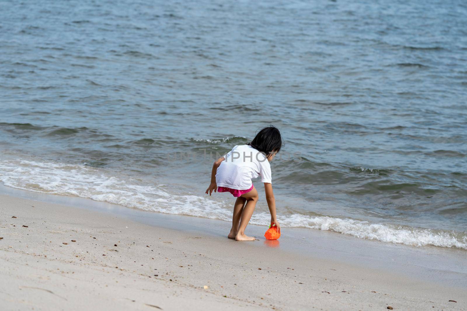 Back of a cute little girl playing with sand on a beach