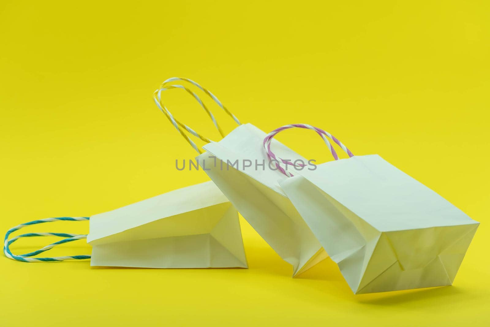 Colourful paper shopping bags isolated on Yellow Background. Closeup shot of white shopping bags