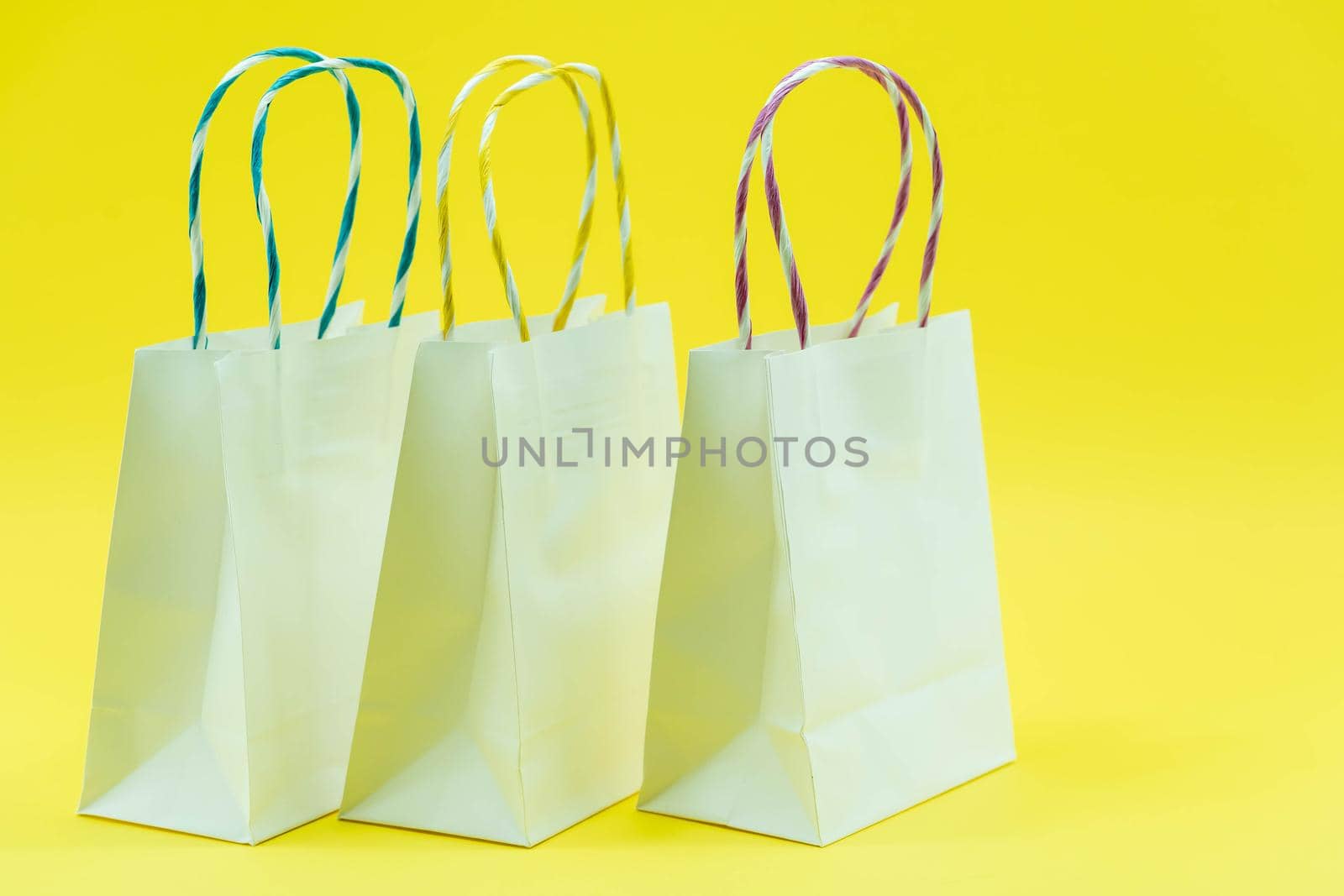 Colourful paper shopping bags isolated on Yellow Background. Closeup shot of white shopping bags