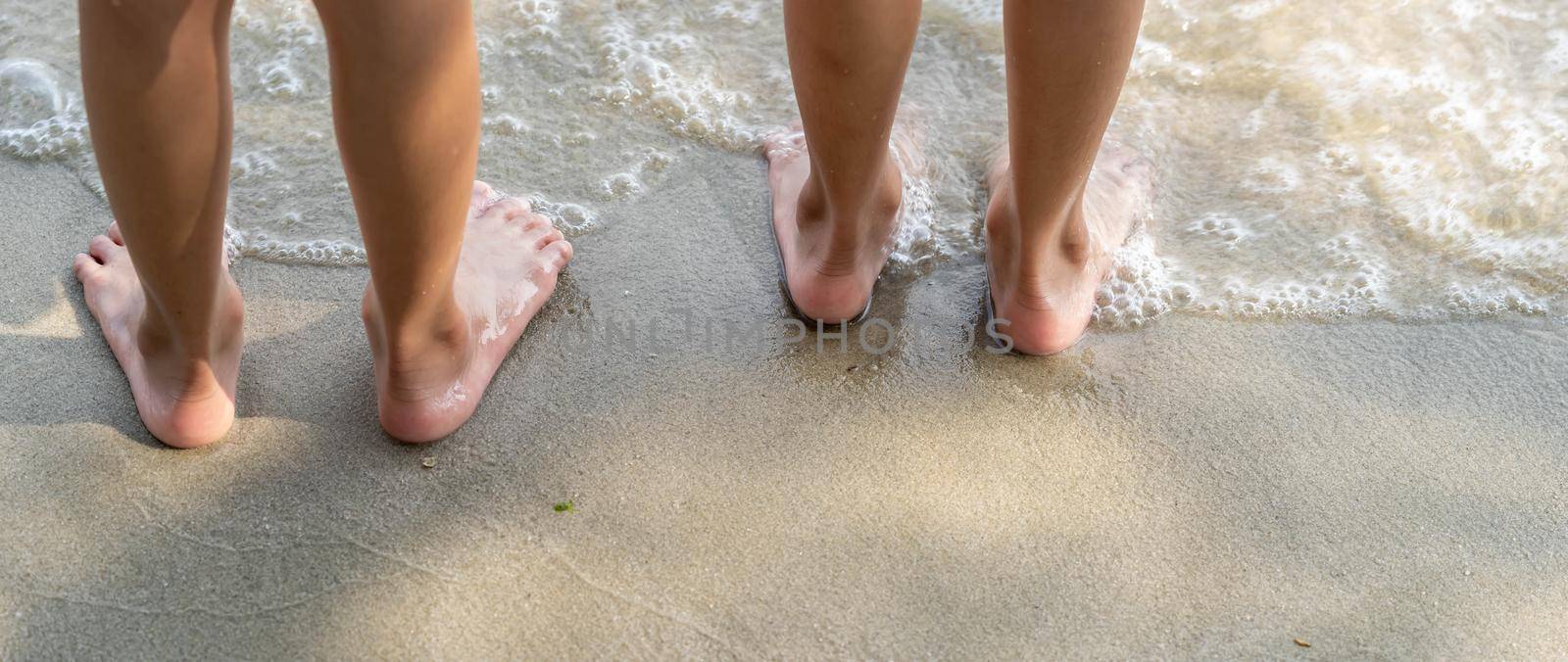 Low angle two child walking barefoot on beach. Feet of children walking barefoot on sand