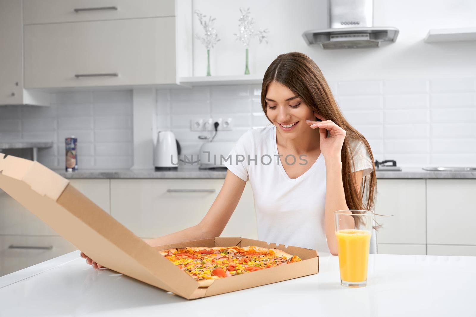 Young woman sitting on table and opening box with pizza. Concept of eating delicious pizza and drinking juice.