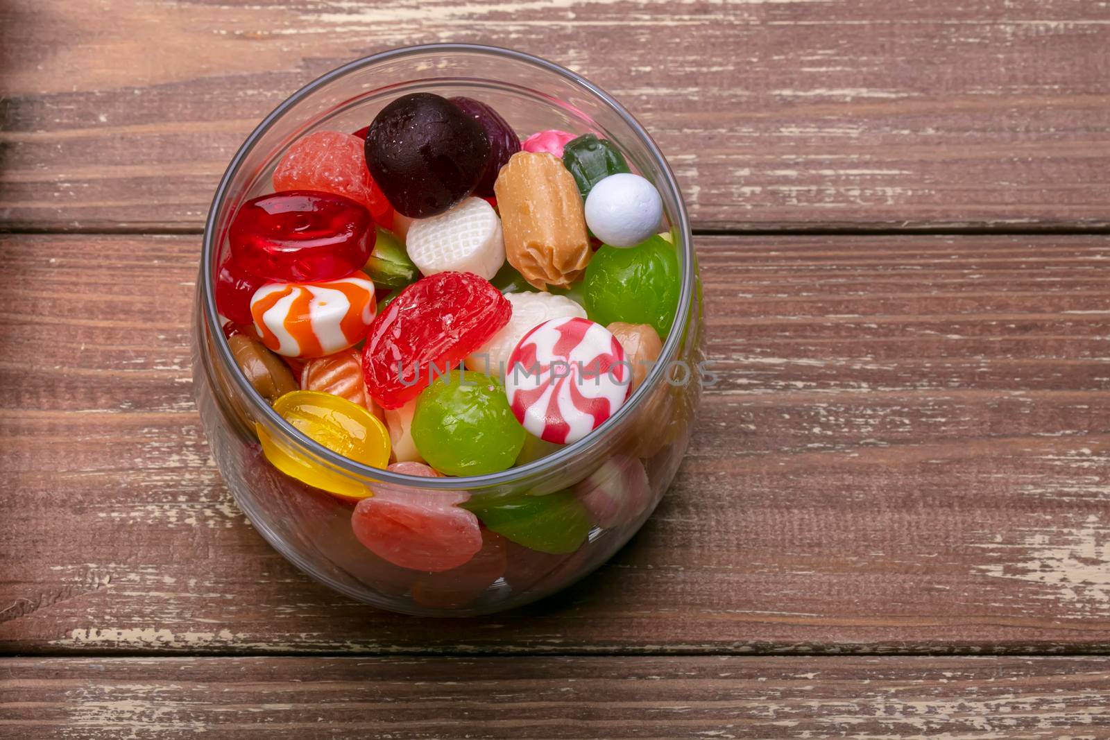 Candies in a jar on a wooden background. Multi-colored caramel. Sweets.