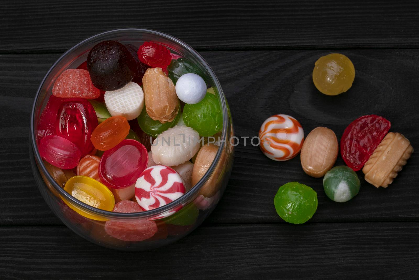 Candies in a jar on a dark background. Multi-colored caramel on a wooden board. Sweets.