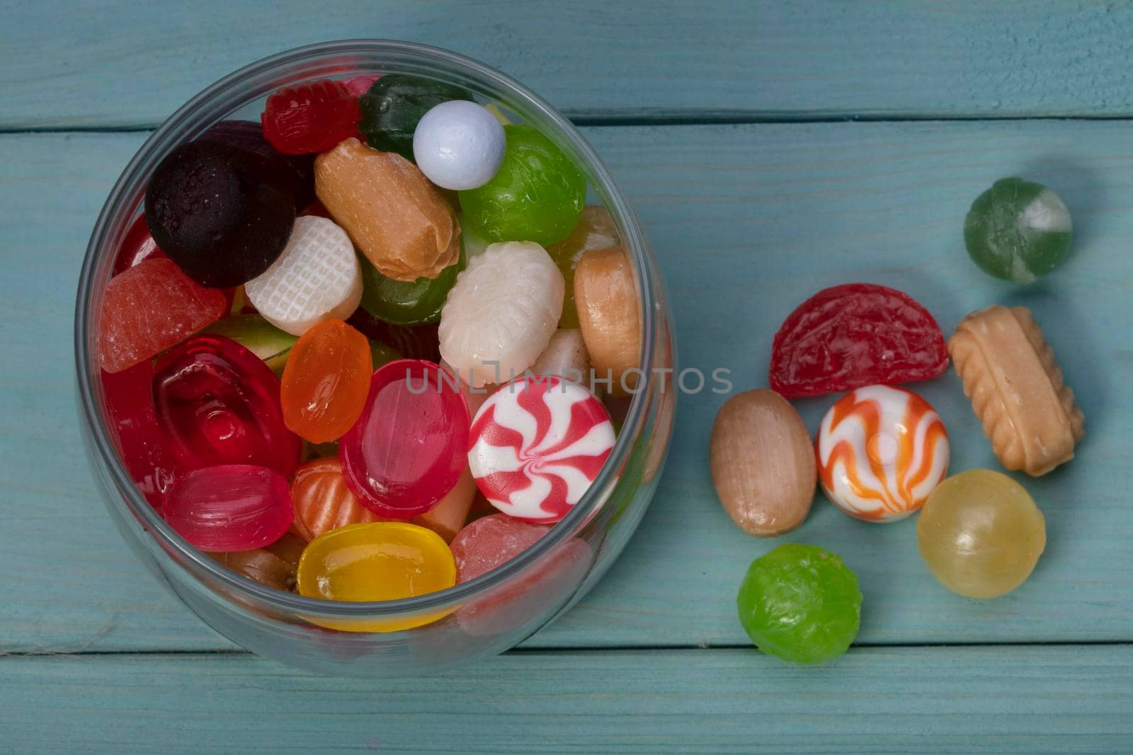 Candies in a jar on a blue background. Multi-colored caramel on a wooden board. Sweets.
