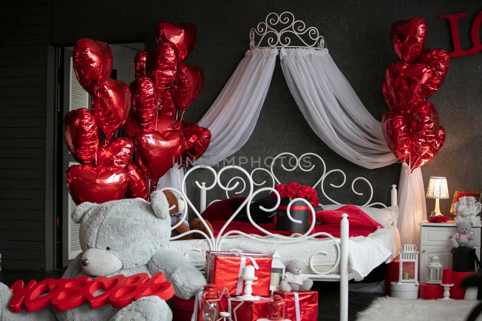 Valentines in the interior. Dark bedroom with a white bed decorated with red balloons. Romantic bedroom interior. Room for the wedding night.