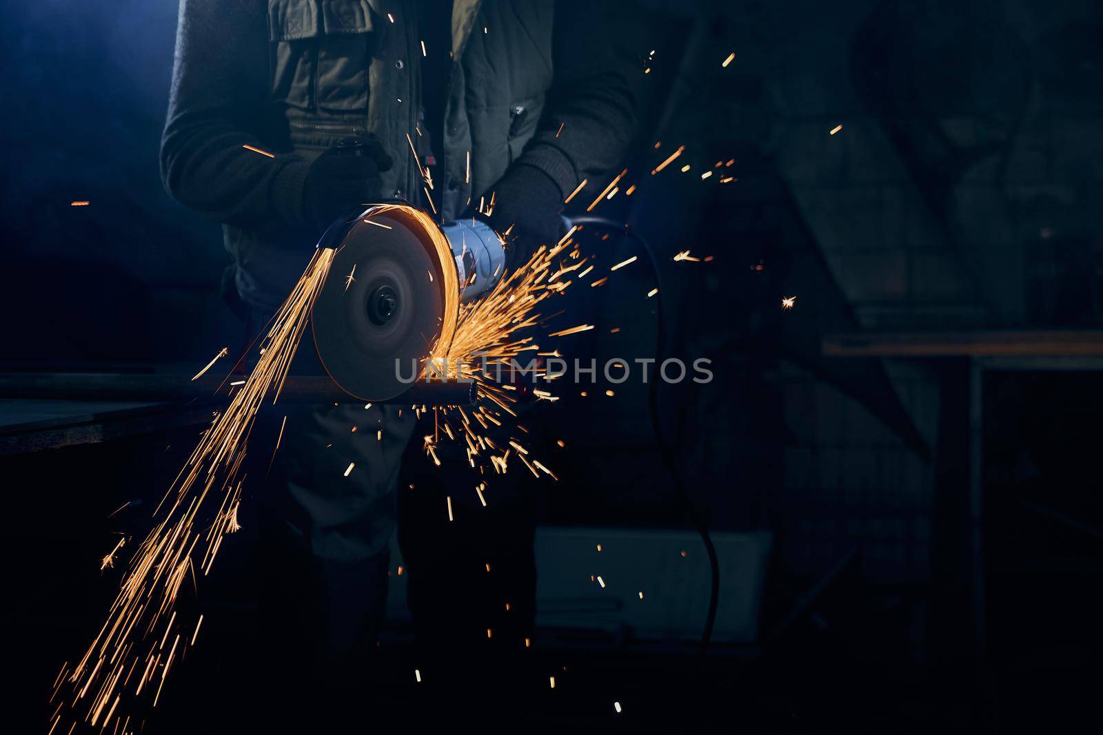 Close up of fitter in special suit cutting with rotating disc for metal with large sparks. Concept of process polishing or welding metal with flash sparks in factory.