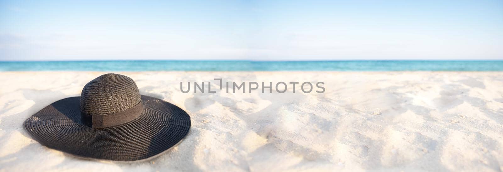 Banner Black hat on a background of the sea. Beach accessory on white sand. Straw panama on the background of the ocean