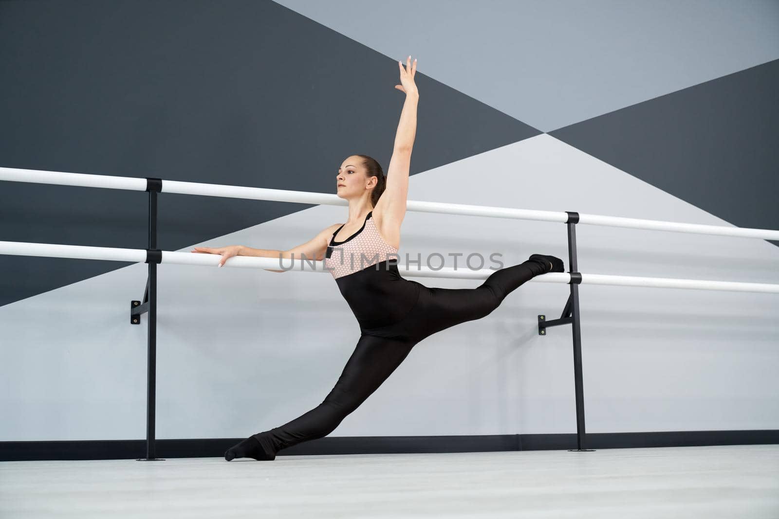 Woman practicing split, holding handrails in dance studio. by SerhiiBobyk