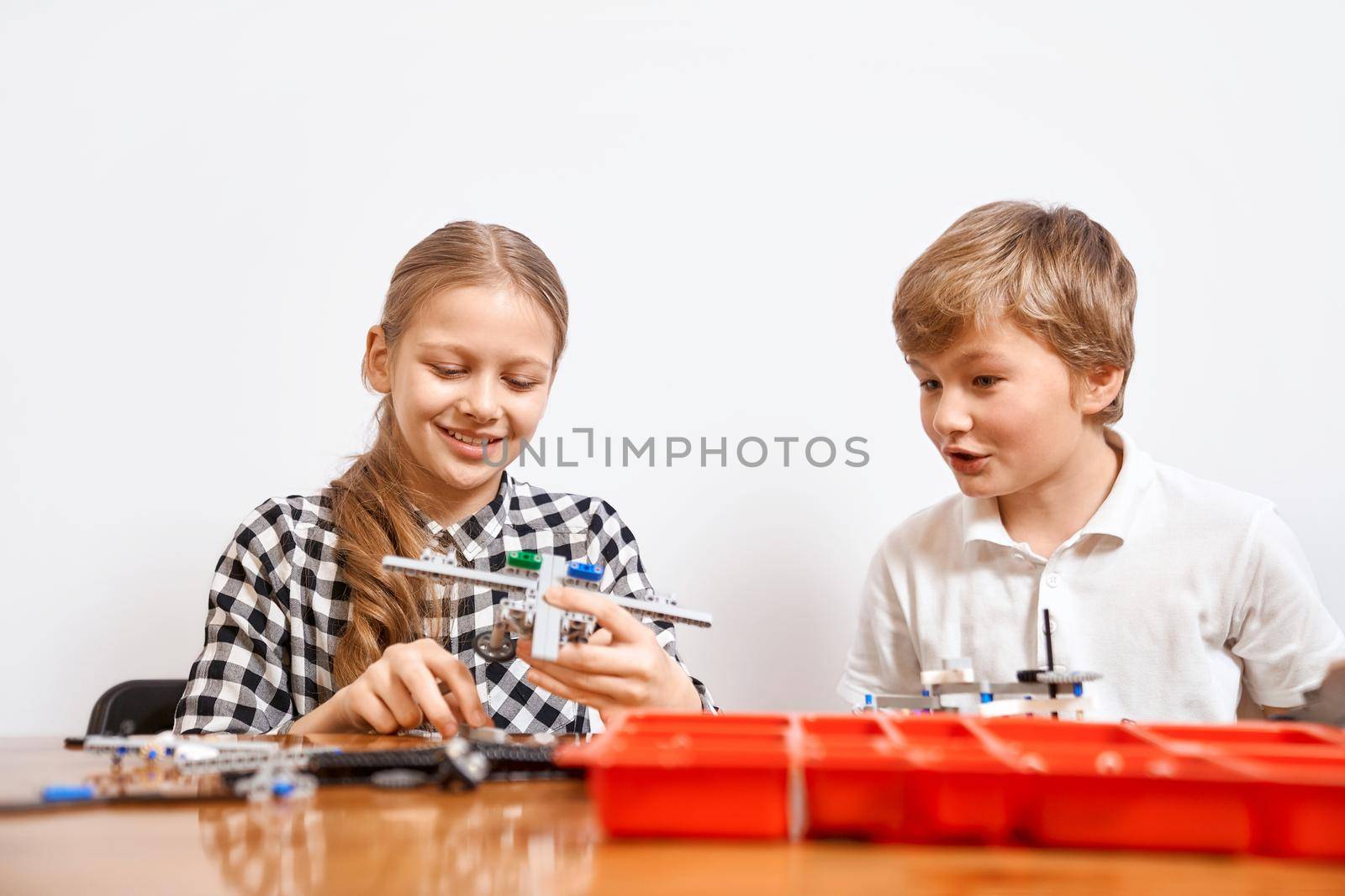 Interesting building kit for kids on table. Front view of boy and girl having fun, creating air vehicle. Science engineering. Nice interested friends smiling, chatting and working on project together.