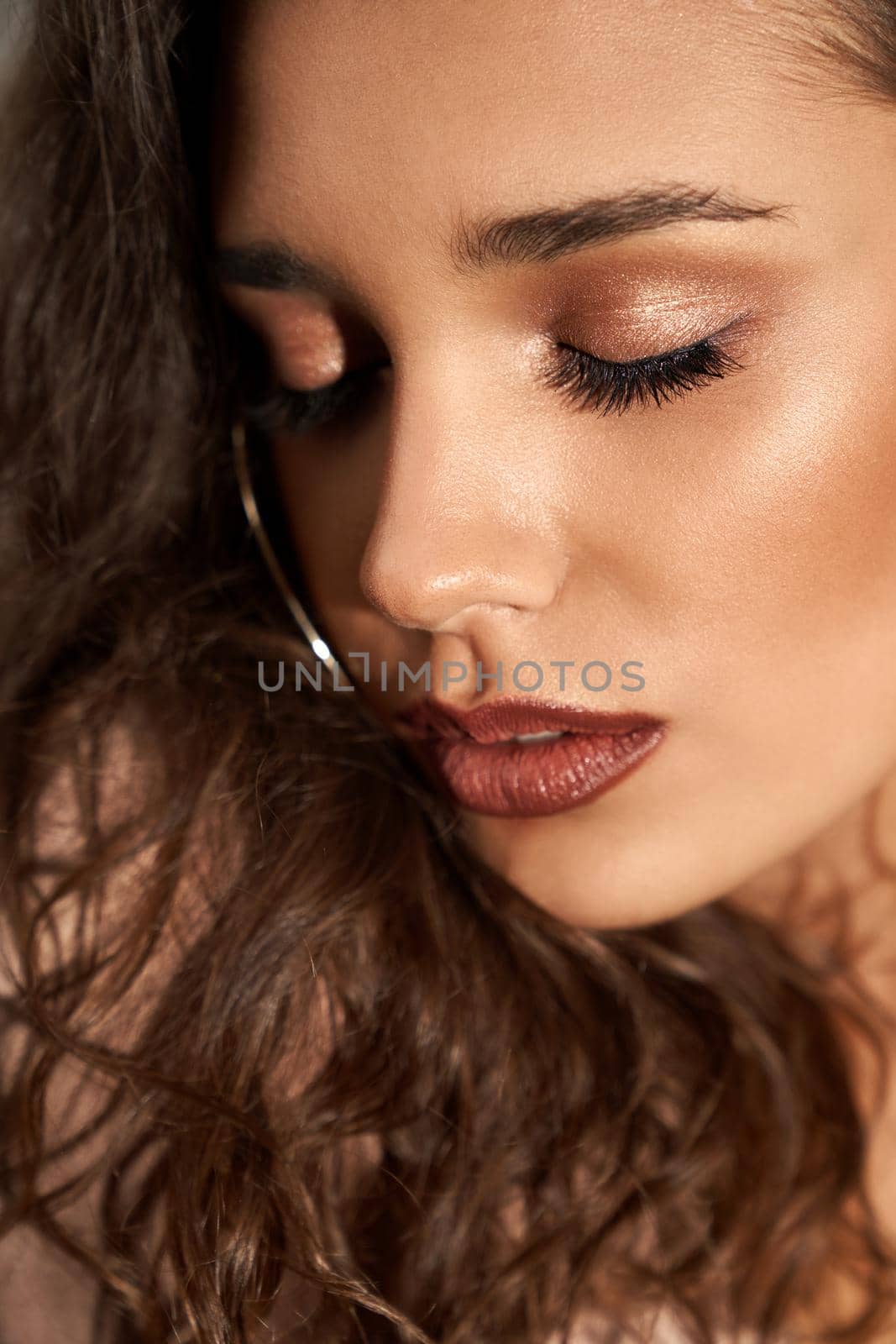 Crop of young caucasian female model with mouth open looking down. Close up portrait of gorgeous woman with curly brown hair, clean skin and perfect make up posing. Concept of beauty.