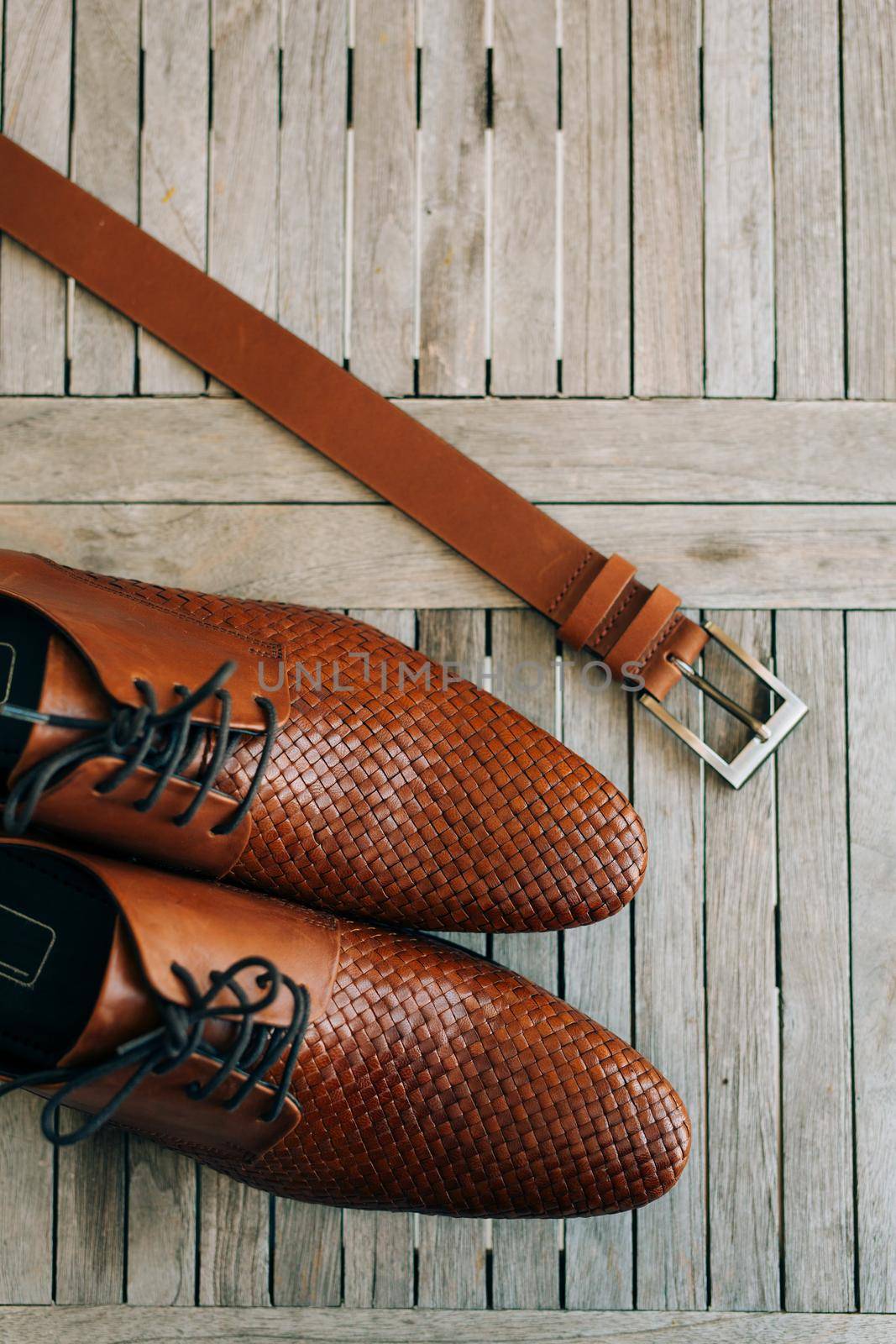 Brown man's shoes with laces on a wooden background and a brown belt.