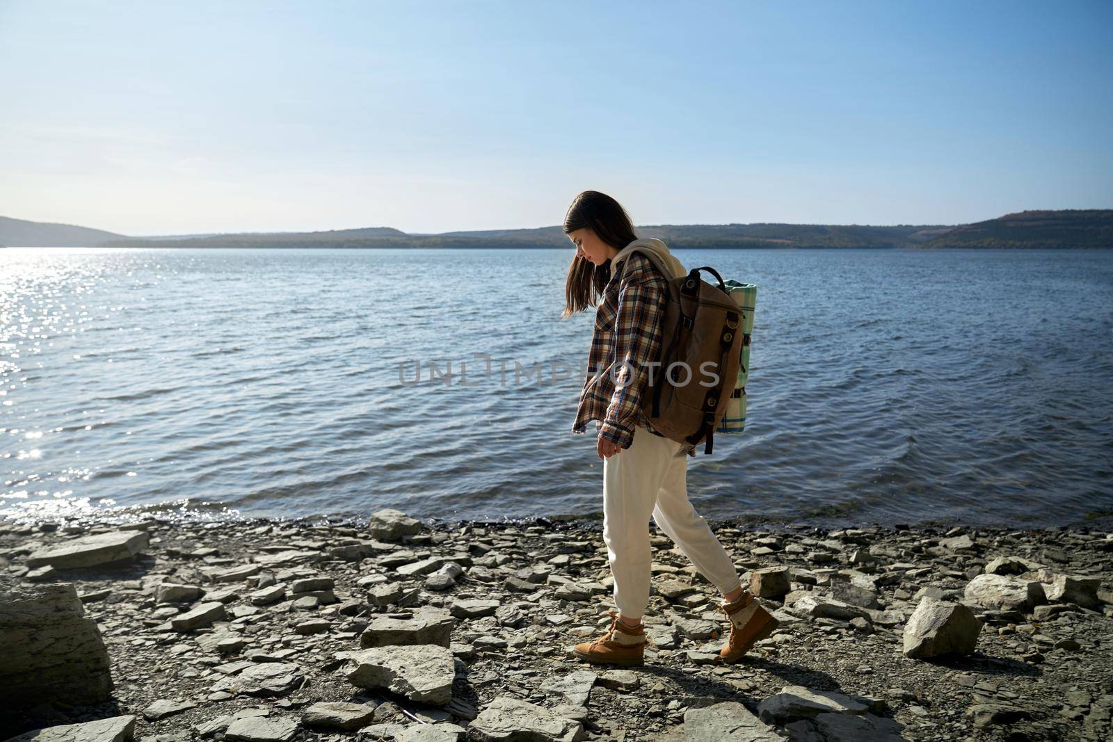 Full length portrait of beautiful young woman in casual wear with backpack walking along riverside. Female tourist discovering new places at national ukrainian park.