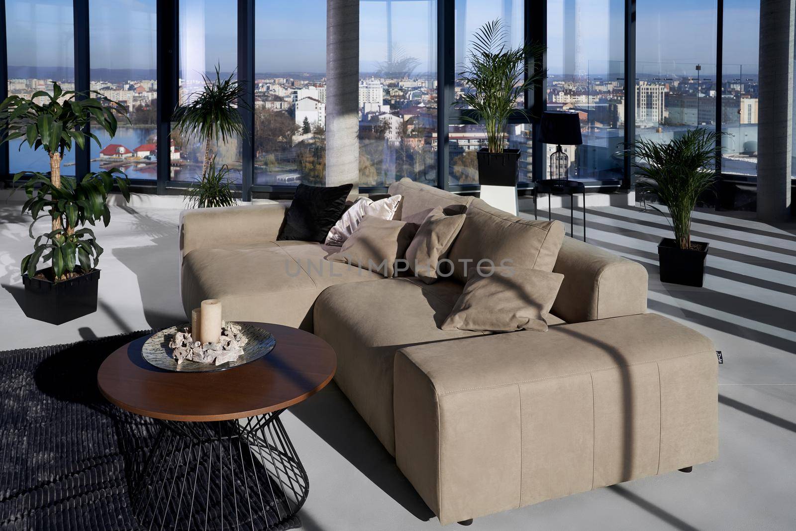 Close up of fashionable leather beige sofa and large panoramic window with incredible view on city. Concept of modern house with beautiful interior and stylish window.