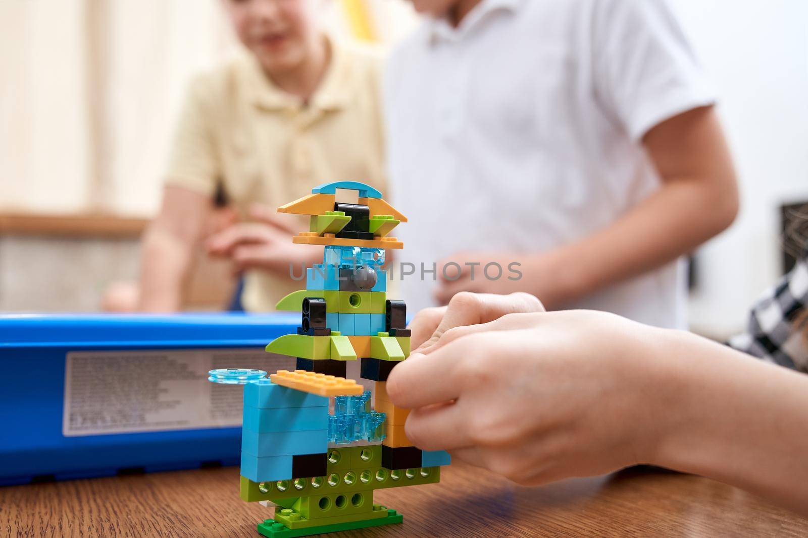 Selective focus of hands using building kit for kids, creating toys. Crop of incognito caucasian child working on project, taking colorful parts. Concept of science engineering.