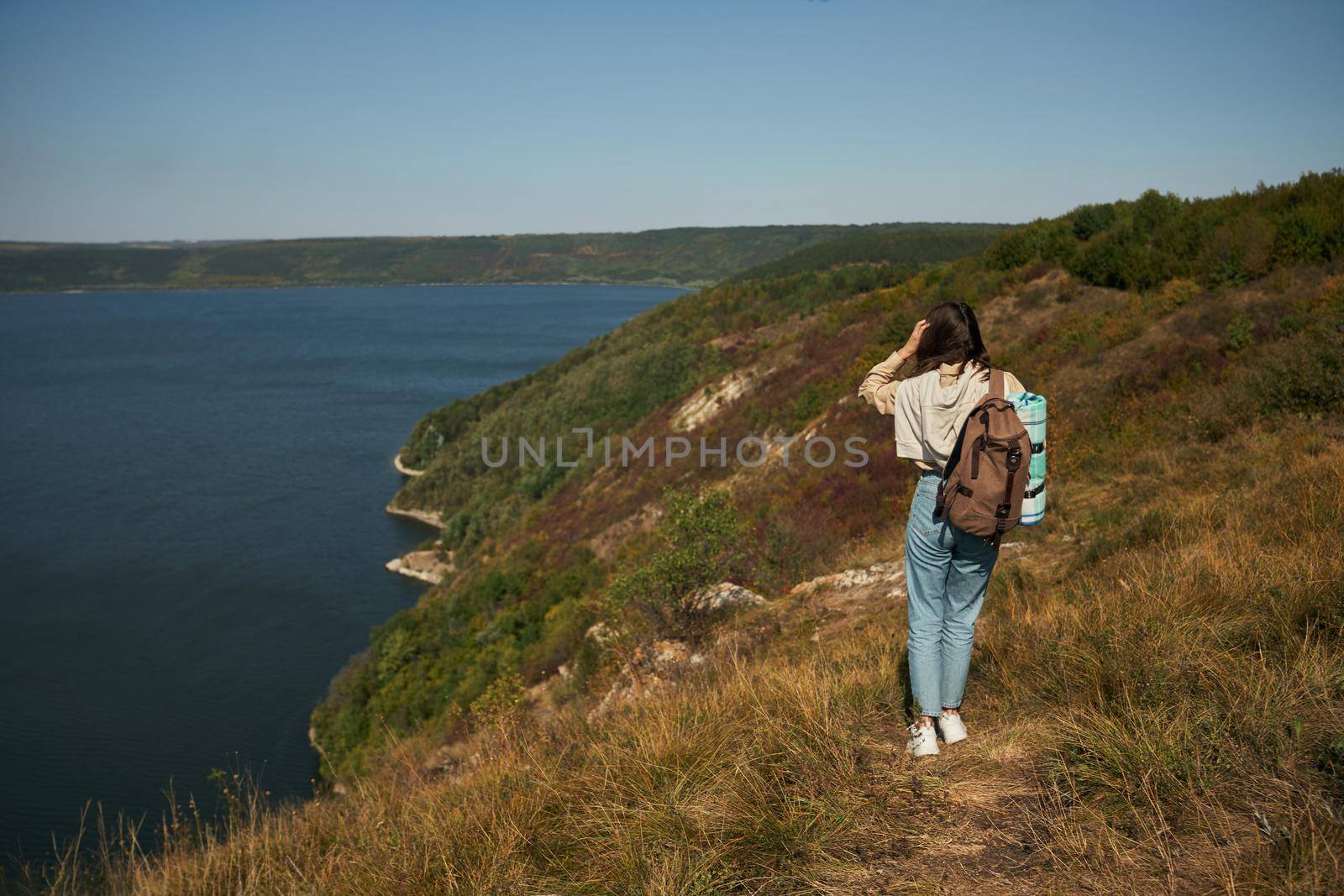 Woman with backpack walking along high green hill by SerhiiBobyk