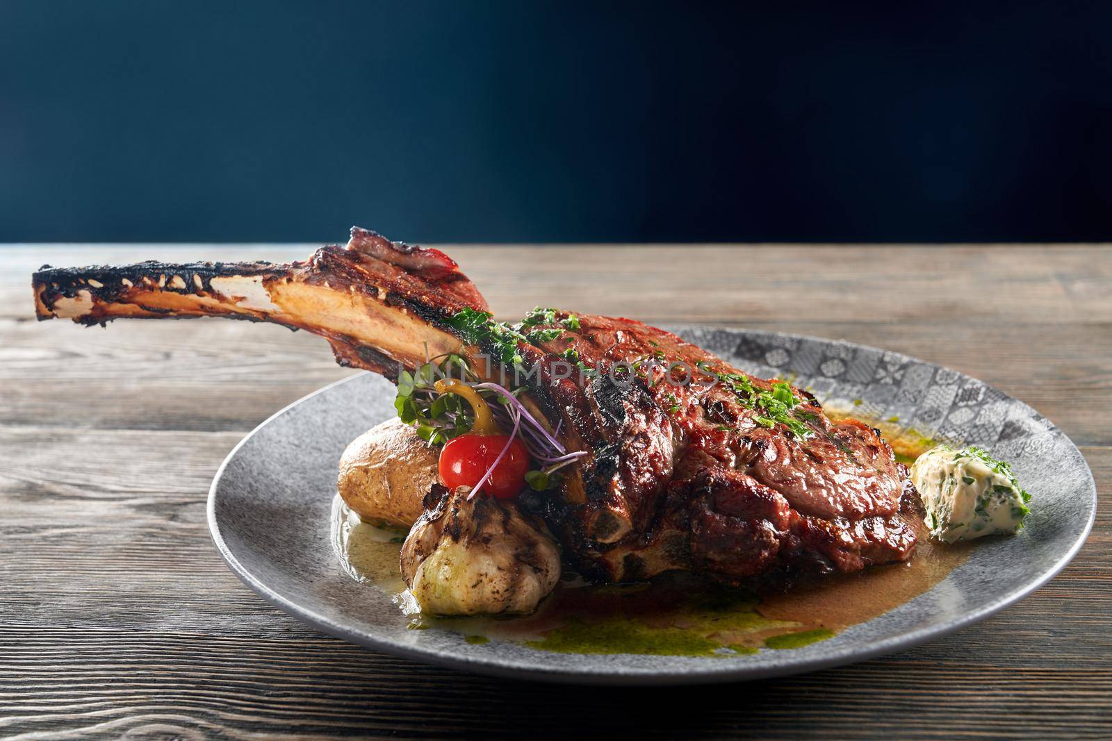 Close up of modern french cuisine. Juicy bbq roasted lamb on bone served with garlic, cheese, vegetables and sauce. Dinner meal isolated on woden table in restaurant. Concept of cuisine, meat.