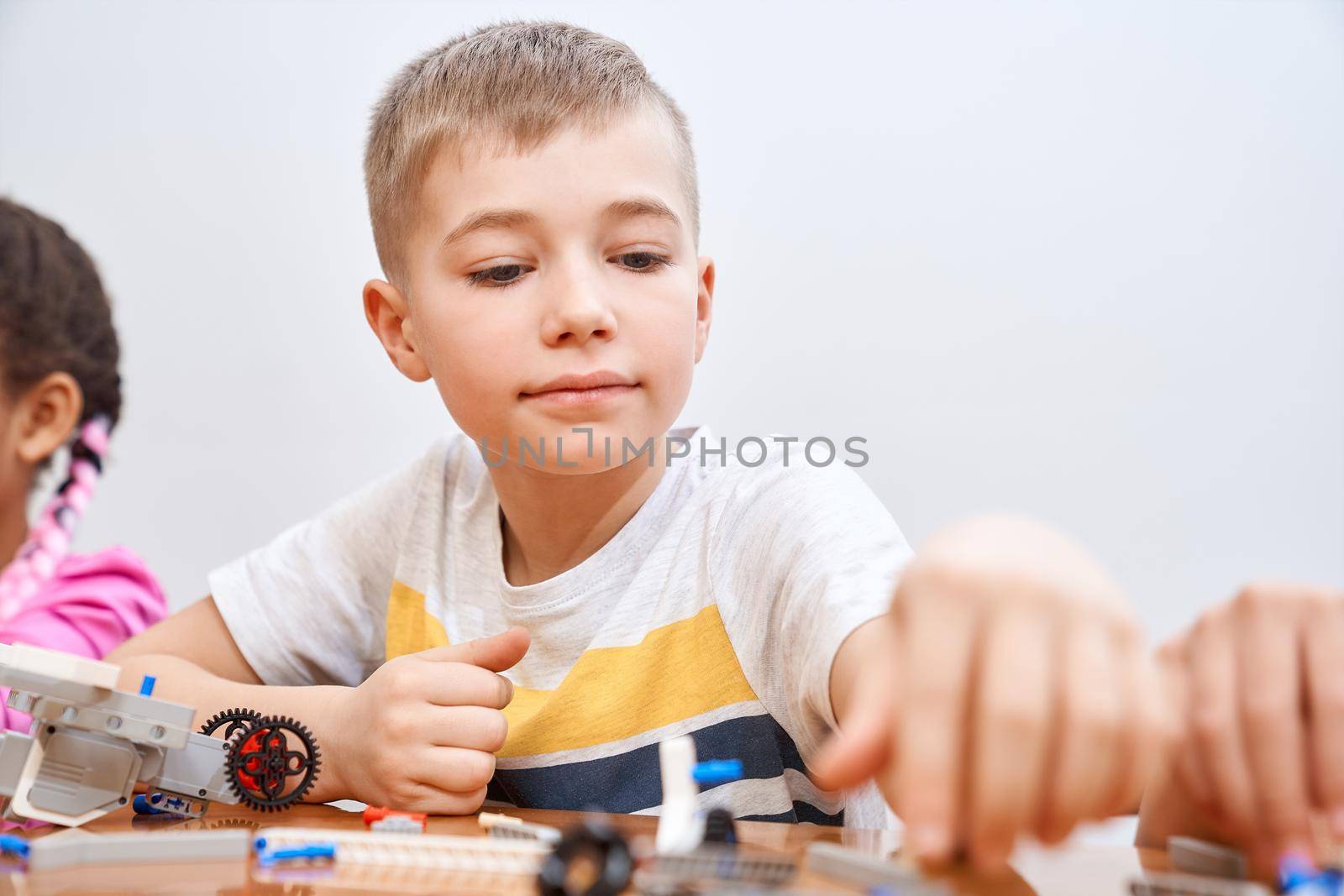 Front view of building kit for group of multiracial kids creating toys, having positive emotions and joy. Selective focus of lovely caucasian boy working on project, taking colorful parts.