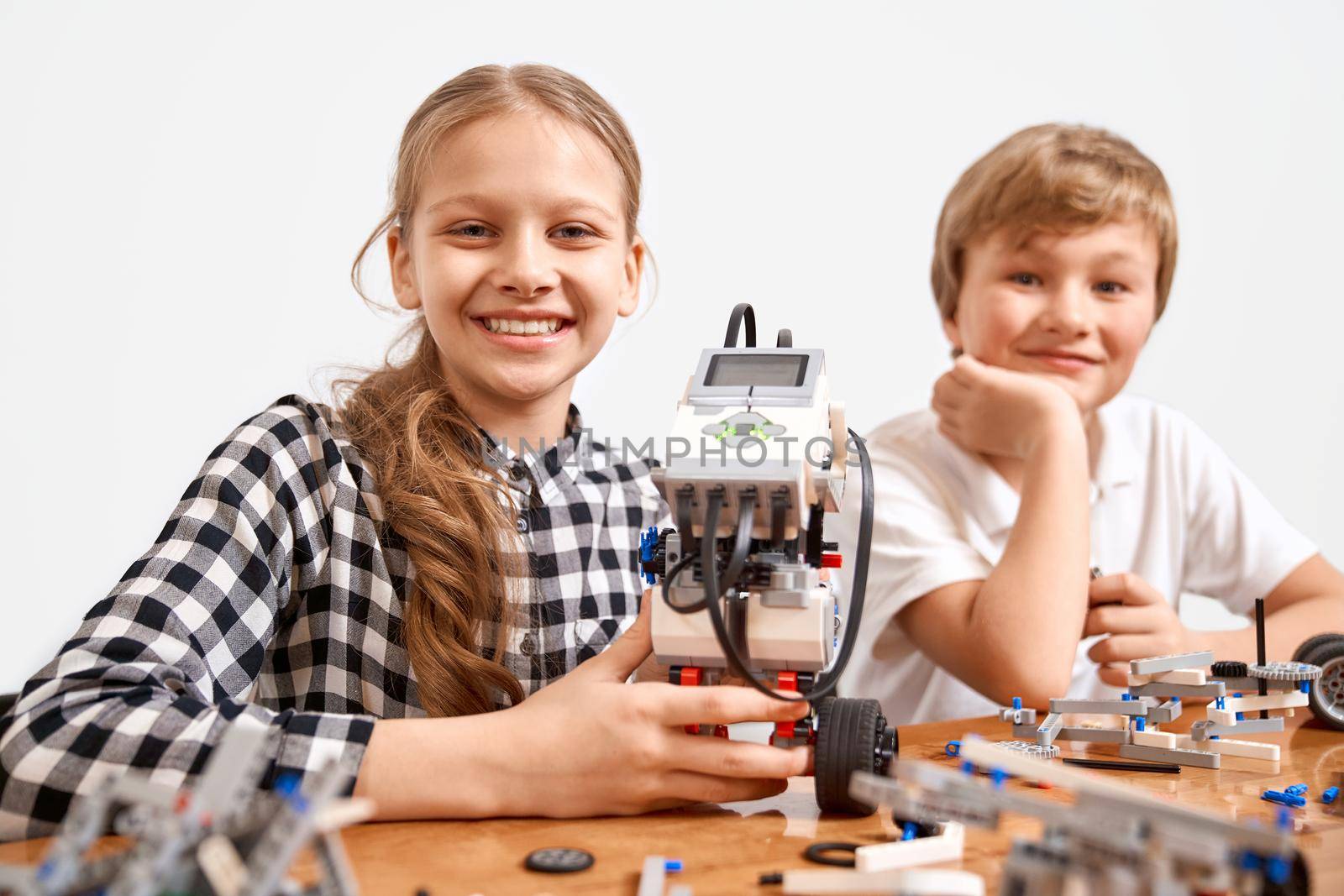 Front view of boy and girl creating robot using building kit for kids on table. Nice interested friends smiling, lookig at camera and working on project together. Concept of science engineering.