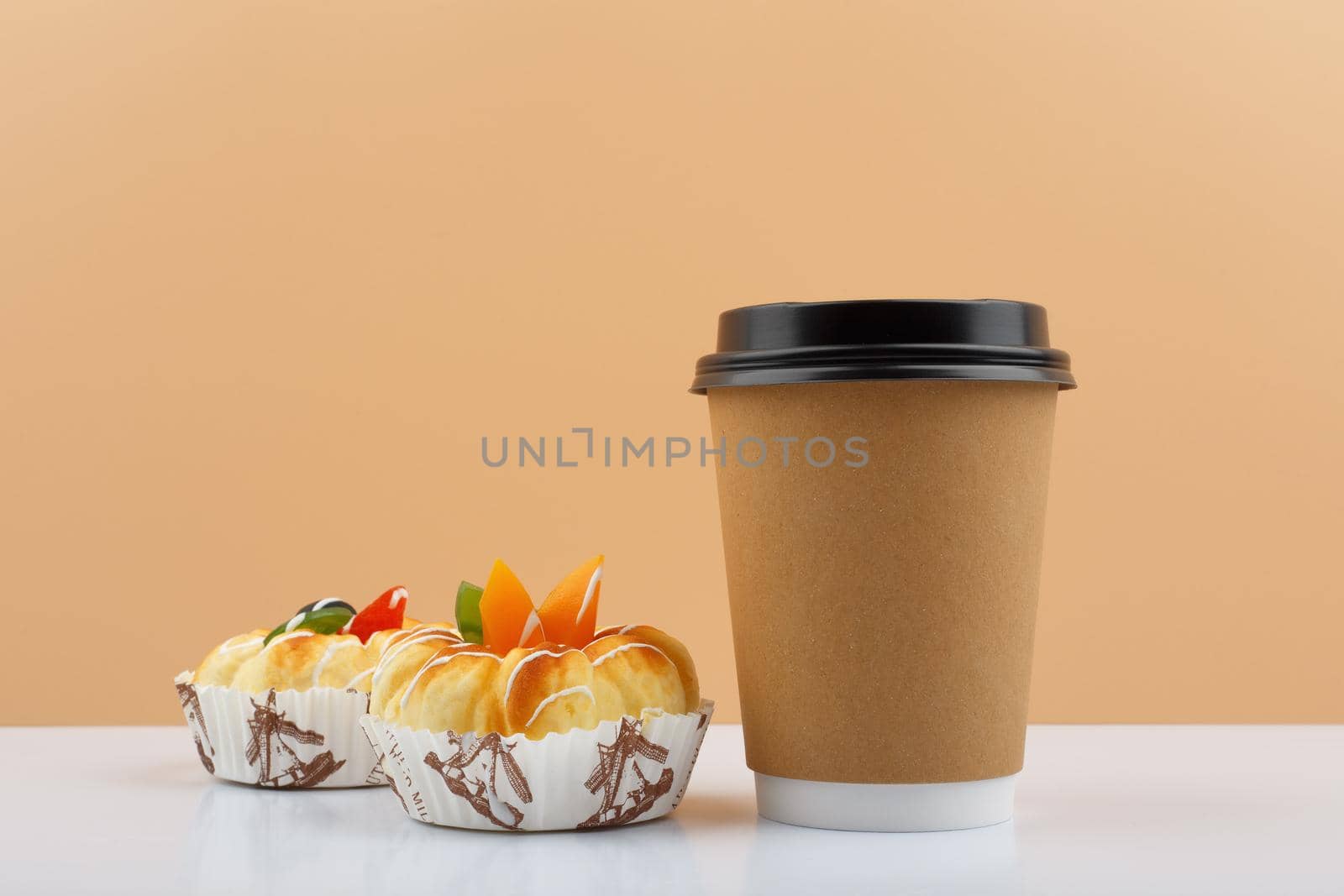 Coffee or tea in cardboard cup with pastry against beige background. Concept of hot drinks and take away food