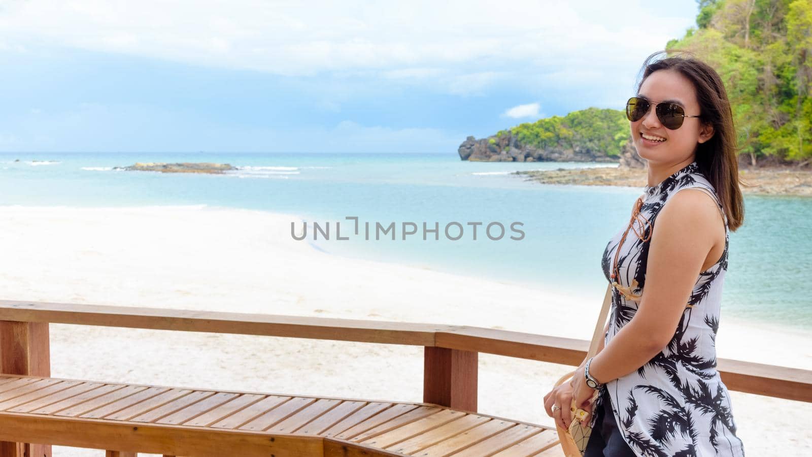 Landscape of the beach and the sea in summer sky and beautiful woman tourist wearing sunglasse, looking at the camera and smiling on Tarutao island, Satun, Thailand, 16:9