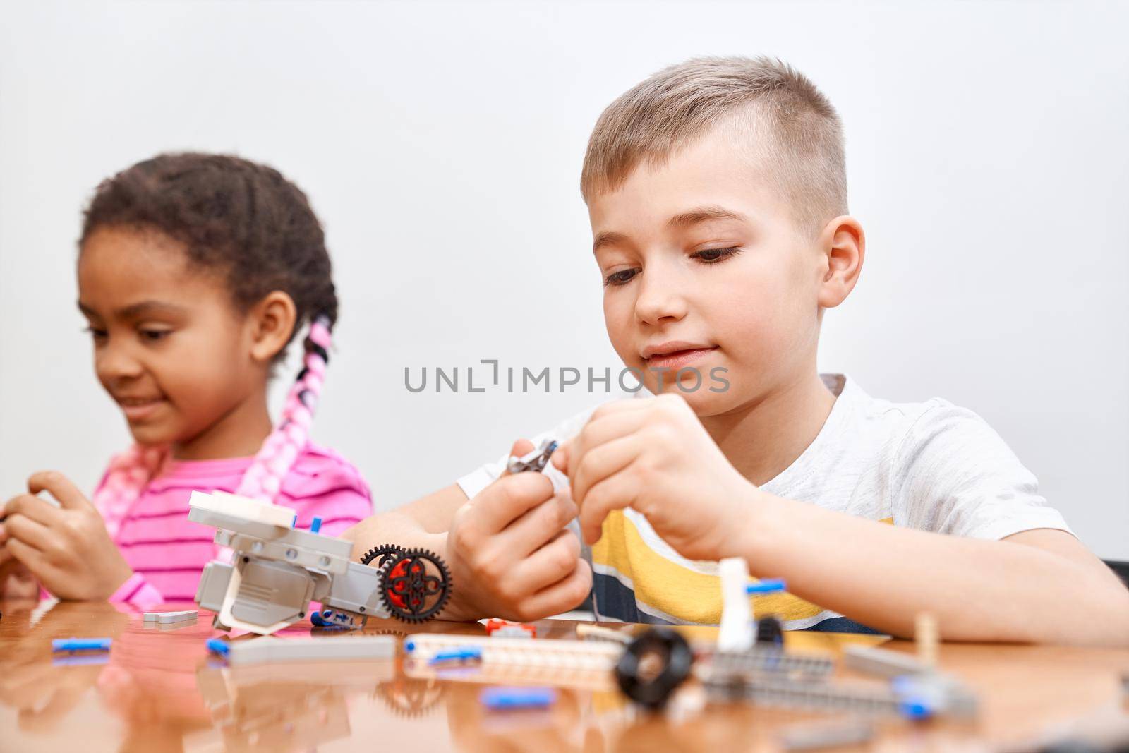 Front view of building kit for group of multiracial kids creating toys, having positive emotions and joy. Selective focus of lovely caucasian boy working on project, taking colorful parts.