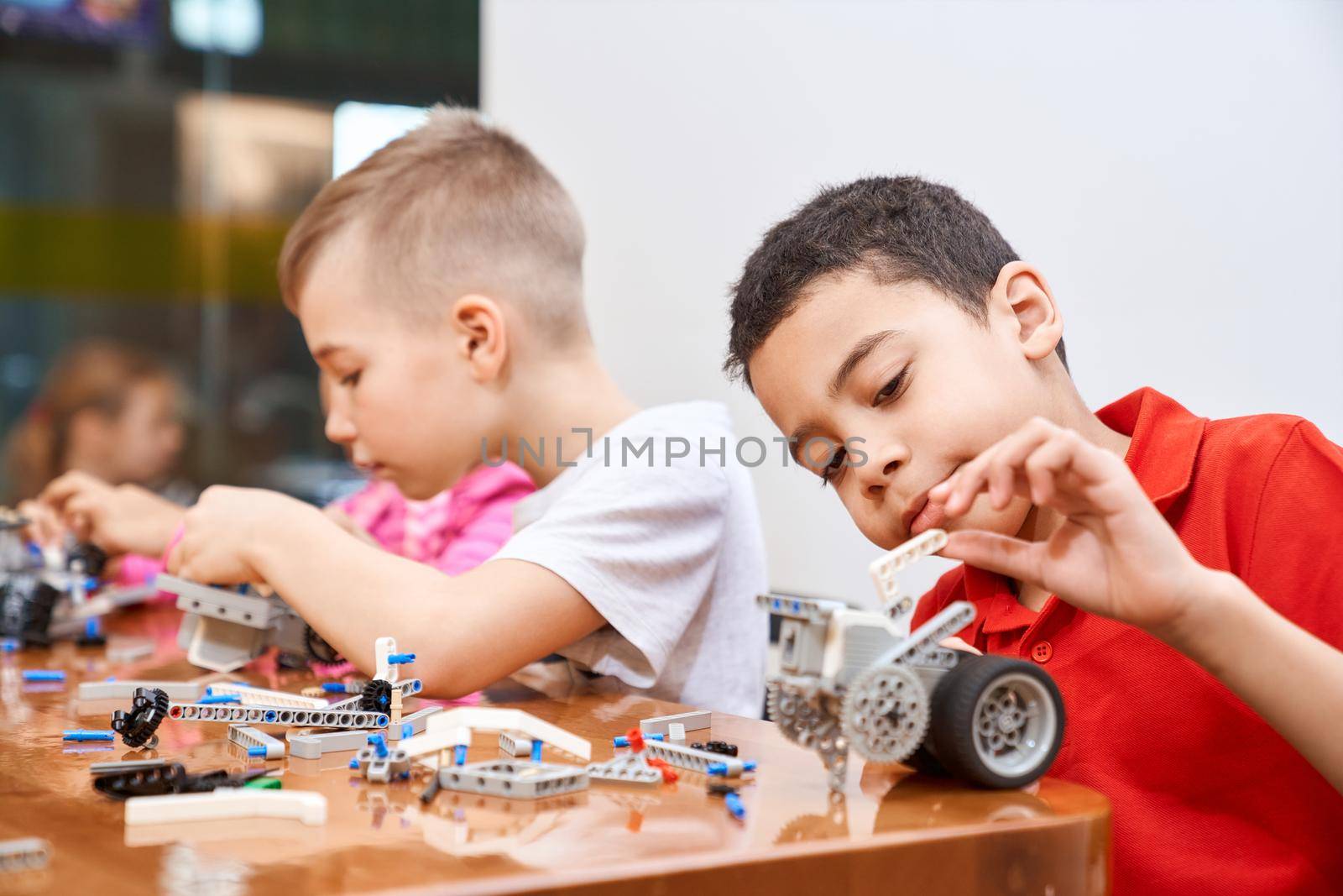 Side view of building kit with colorful pieces in box for group of multiracial kids creating robots, having positive emotions and joy. Close up of interested friends working on project.